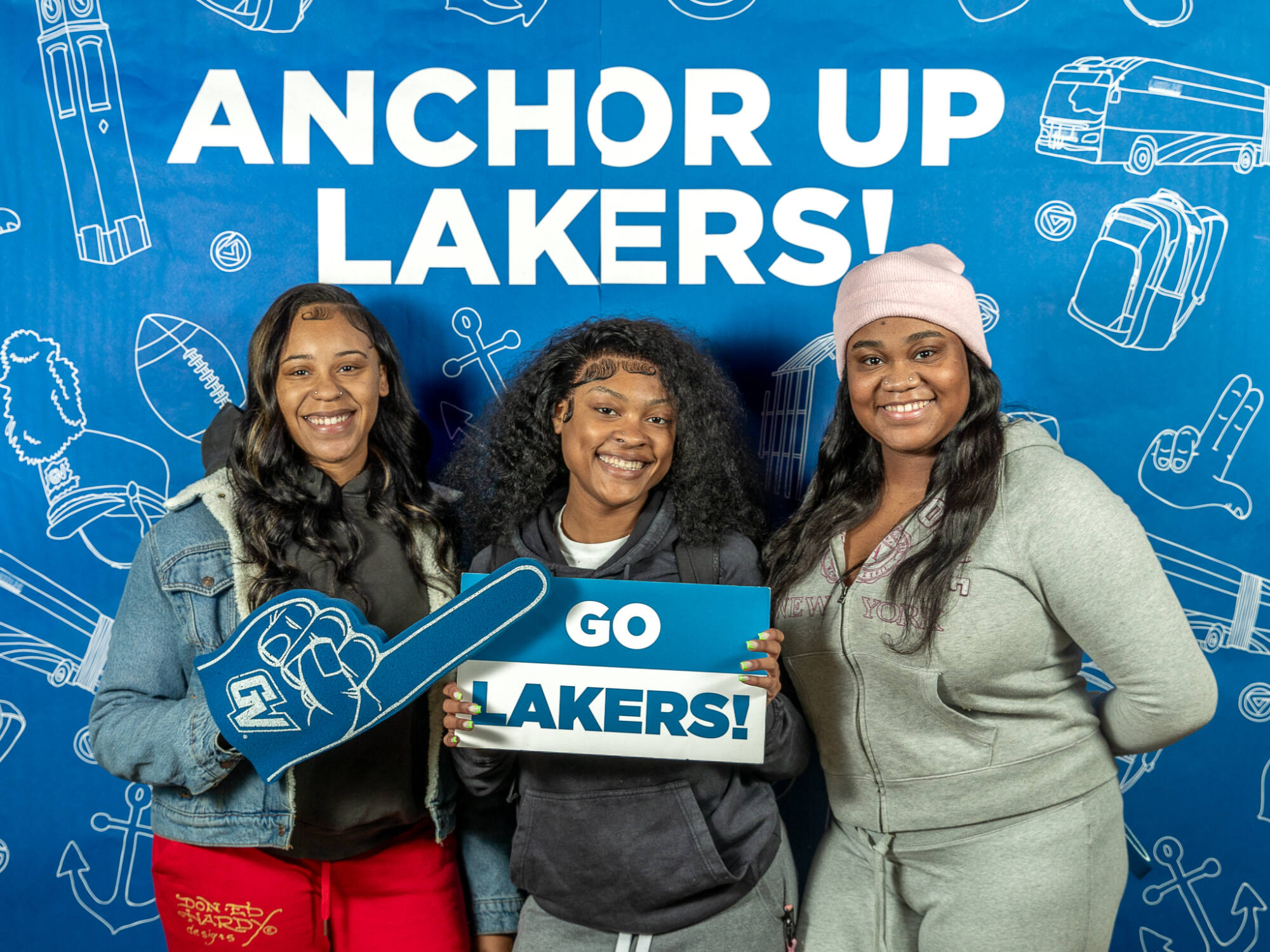 three individuals, one on the left holding up a foam finger, one in the middle holding up a Go Lakers! sign, one on the right with hands behind their back
